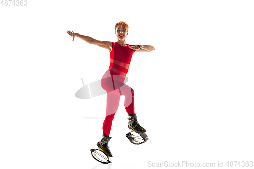 Image of Beautiful redhead woman in a red sportswear jumping in a kangoo jumps shoes isolated on white studio background.