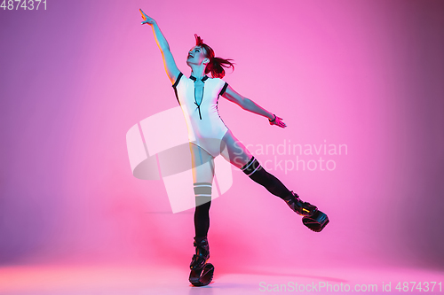 Image of Beautiful redhead woman in a white sportswear jumping in a kangoo jumps shoes isolated on gradient studio background in neon light