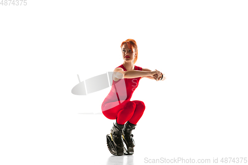 Image of Beautiful redhead woman in a red sportswear jumping in a kangoo jumps shoes isolated on white studio background.