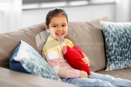 Image of happy little girl with heart shaped pillow at home