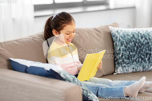 Image of happy smiling little girl reading book at home