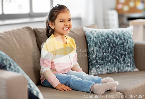 Image of happy smiling little girl sitting on sofa at home