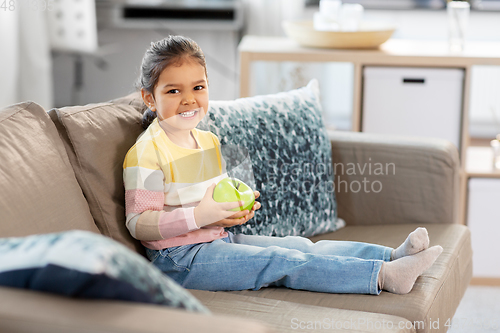 Image of happy little girl with apple sitting on sofa