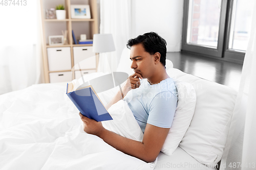 Image of indian man reading book in bed at home