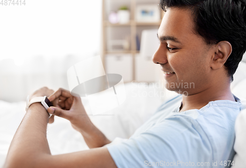 Image of happy indian man with smart watch in bed at home