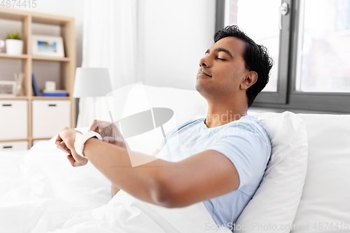 Image of happy indian man with smart watch in bed at home