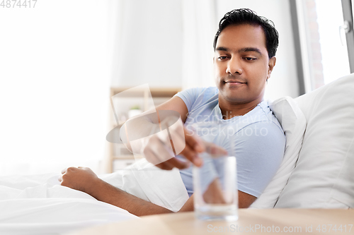 Image of happy indian man drinking water lying in bed