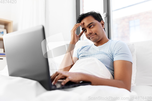 Image of bored indian man with laptop in bed at home