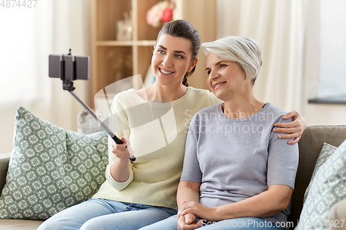 Image of senior mother with daughter taking selfie at home