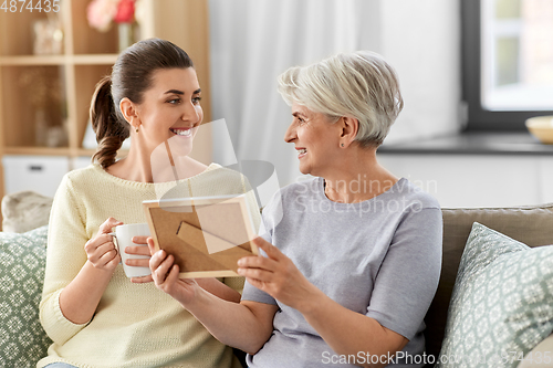 Image of adult daughter and old mother with photo at home