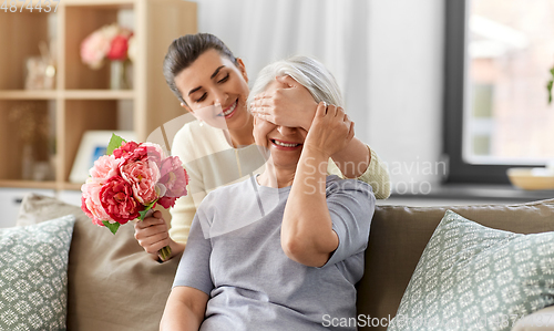 Image of adult daughter giving flowers to old mother