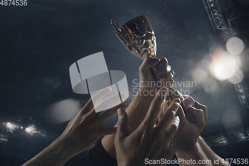 Image of Award of victory, male hands tightening the cup of winners against cloudy dark sky