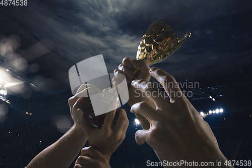 Image of Award of victory, male hands tightening the cup of winners against cloudy dark sky