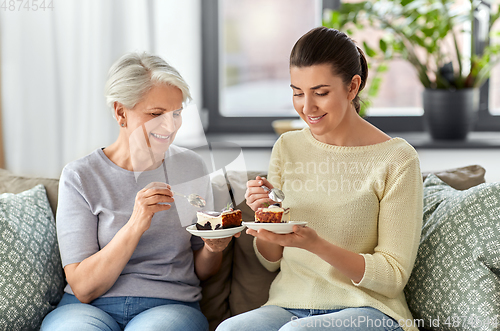 Image of old mother and adult daughter eating cake at home