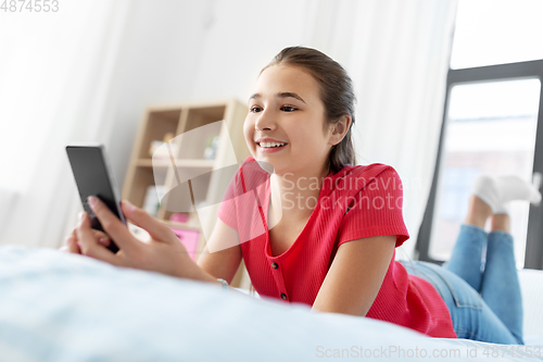 Image of smiling teenage girl texting on smartphone at home