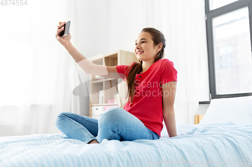 Image of happy girl with smartphone taking selfie at home