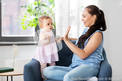 Image of happy mother playing with baby daughter at home