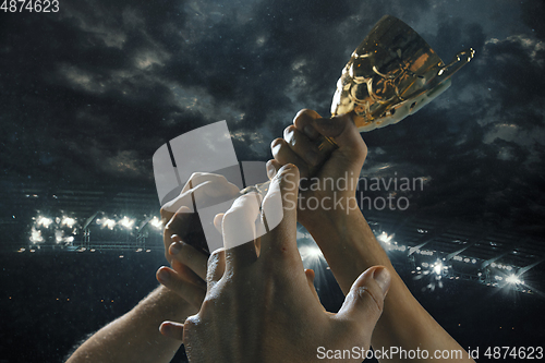 Image of Award of victory, male hands tightening the cup of winners against cloudy dark sky