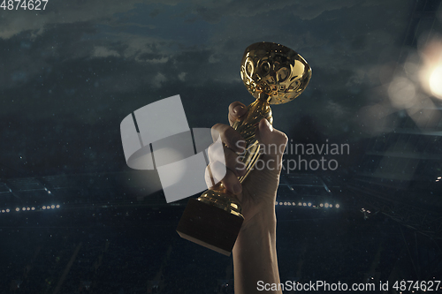 Image of Award of victory, male hands tightening the cup of winners against cloudy dark sky