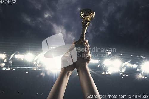 Image of Award of victory, male hands tightening the cup of winners against cloudy dark sky