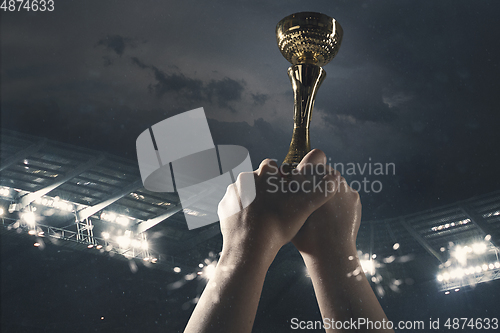 Image of Award of victory, male hands tightening the cup of winners against cloudy dark sky