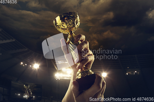 Image of Award of victory, male hands tightening the cup of winners against cloudy dark sky