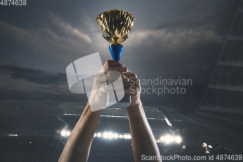 Image of Award of victory, male hands tightening the cup of winners against cloudy dark sky