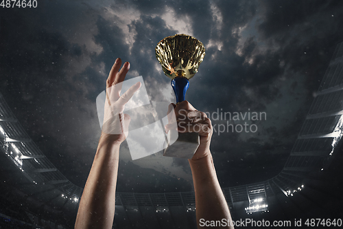 Image of Award of victory, male hands tightening the cup of winners against cloudy dark sky