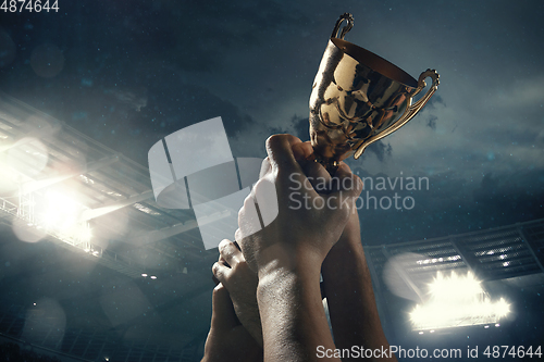 Image of Award of victory, male hands tightening the cup of winners against cloudy dark sky