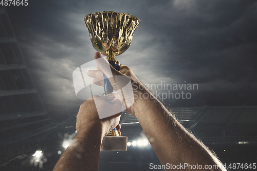 Image of Award of victory, male hands tightening the cup of winners against cloudy dark sky