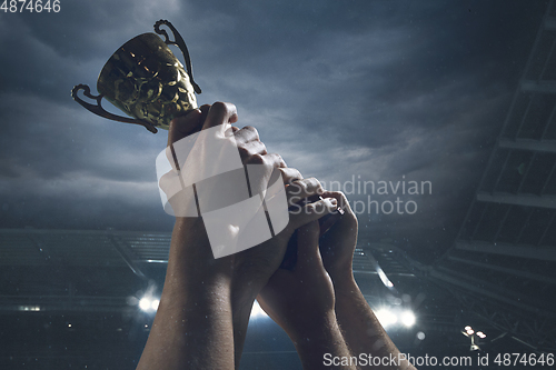 Image of Award of victory, male hands tightening the cup of winners against cloudy dark sky