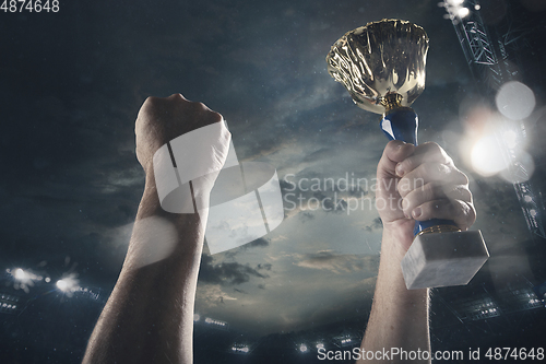 Image of Award of victory, male hands tightening the cup of winners against cloudy dark sky