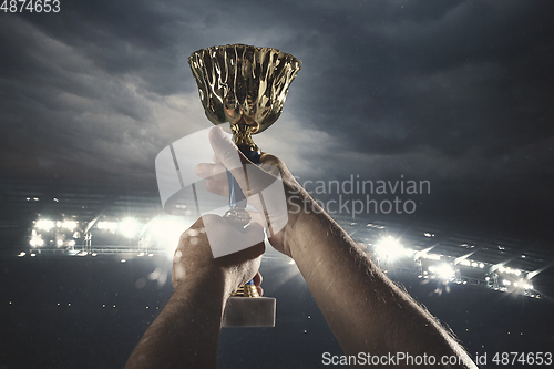 Image of Award of victory, male hands tightening the cup of winners against cloudy dark sky