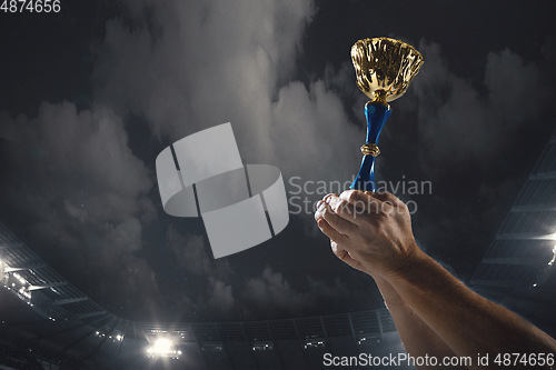 Image of Award of victory, male hands tightening the cup of winners against cloudy dark sky