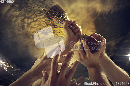 Image of Award of victory, male hands tightening the cup of winners against cloudy dark sky