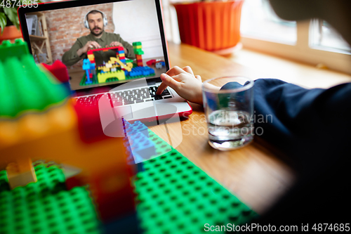 Image of Girl playing with constructor at home, watching teacher\'s tutorial on laptop. Digitalization, remote education