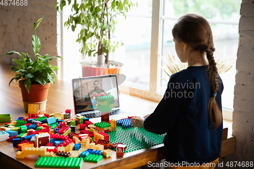 Image of Girl playing with constructor at home, watching teacher\'s tutorial on laptop. Digitalization, remote education