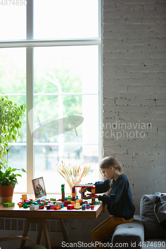 Image of Girl playing with constructor at home, watching teacher\'s tutorial on laptop. Digitalization, remote education