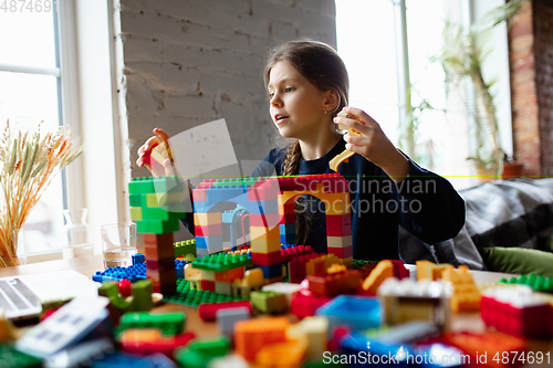 Image of Girl playing with constructor at home, watching teacher\'s tutorial on laptop. Digitalization, remote education