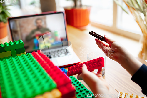 Image of Girl playing with constructor at home, watching teacher\'s tutorial on laptop. Digitalization, remote education