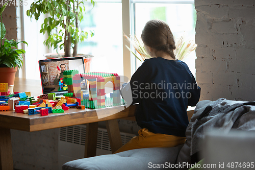 Image of Girl playing with constructor at home, watching teacher\'s tutorial on laptop. Digitalization, remote education