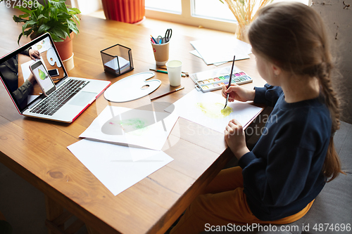 Image of Girl drawing with paints and pencils at home, watching teacher\'s tutorial on laptop. Digitalization, remote education