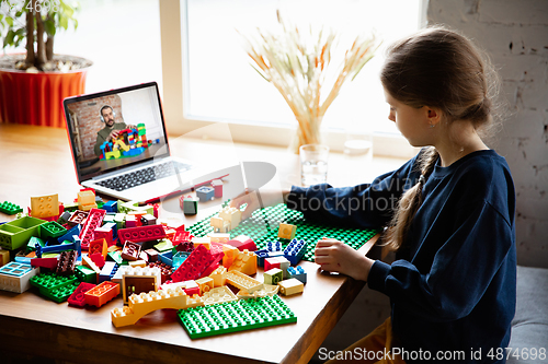 Image of Girl playing with constructor at home, watching teacher\'s tutorial on laptop. Digitalization, remote education