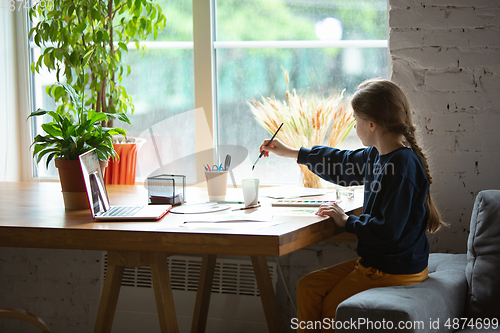 Image of Girl drawing with paints and pencils at home, watching teacher\'s tutorial on laptop. Digitalization, remote education