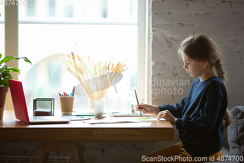 Image of Girl drawing with paints and pencils at home, watching teacher\'s tutorial on laptop. Digitalization, remote education