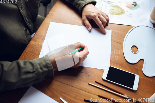 Image of Close up of man drawing with paints and pencils at home. Remote education, creative occupation, art therapy