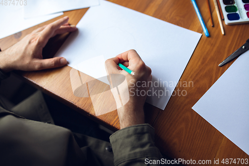 Image of Close up of man drawing with paints and pencils at home. Remote education, creative occupation, art therapy