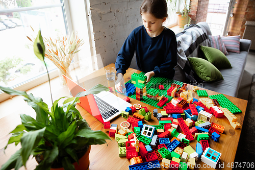 Image of Girl playing with constructor at home, watching teacher\'s tutorial on laptop. Digitalization, remote education