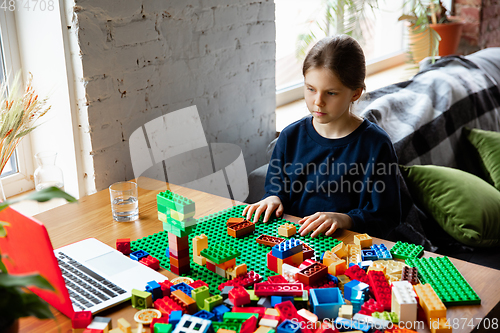 Image of Girl playing with constructor at home, watching teacher\'s tutorial on laptop. Digitalization, remote education