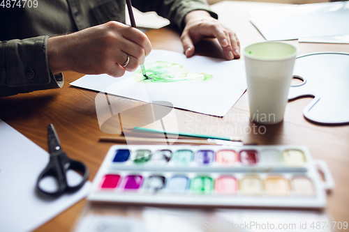 Image of Close up of man drawing with paints and pencils at home. Remote education, creative occupation, art therapy